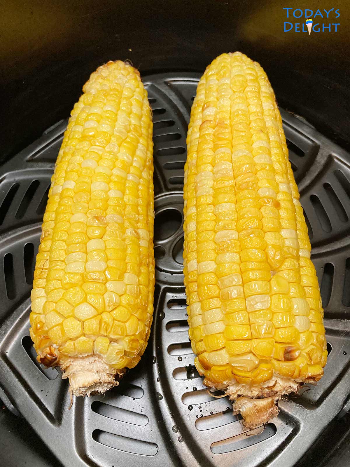 Two cooked corn in the cob in air fryer basket.