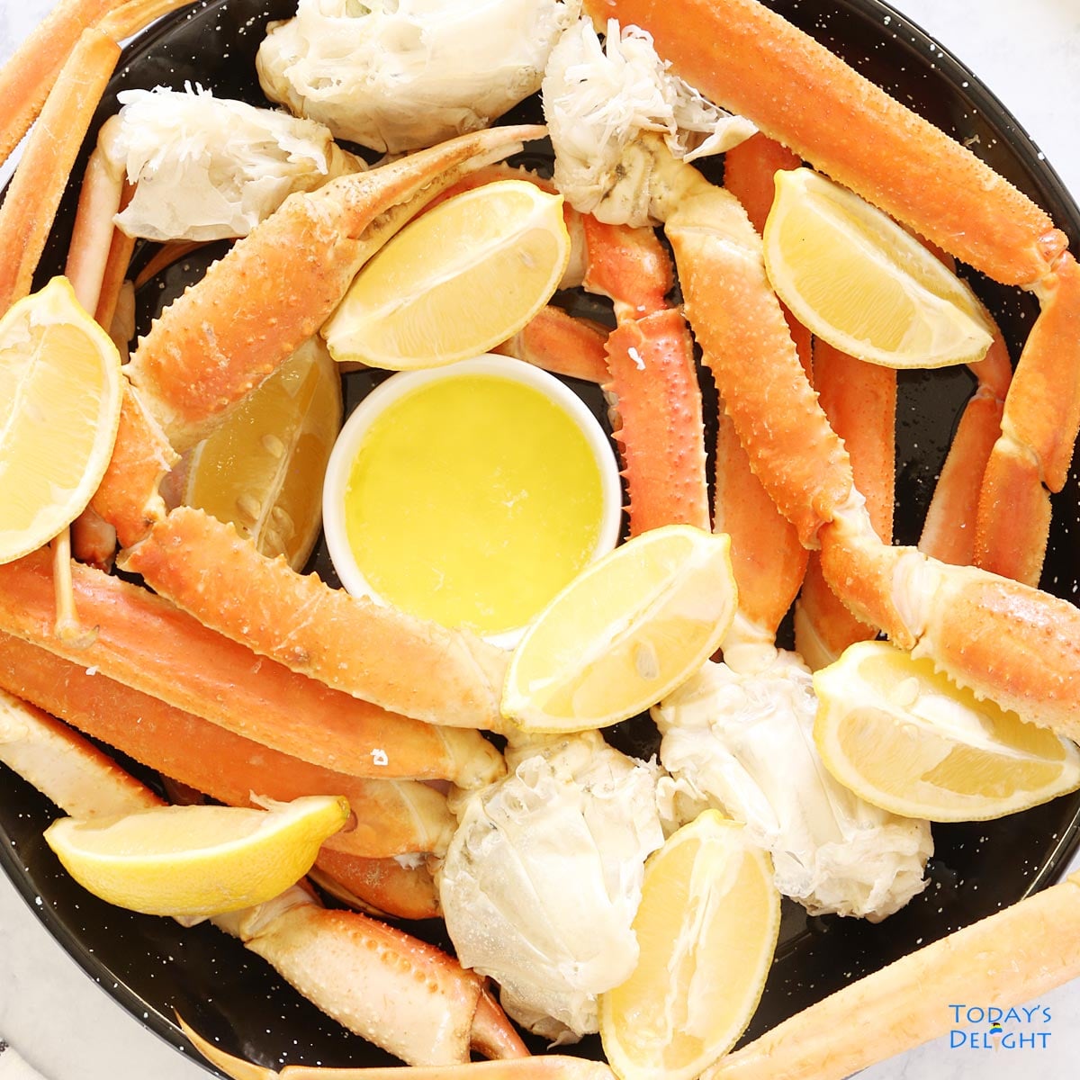 Two pounds of steamed snow crab legs on a platter with lemon wedges and melted butter. 