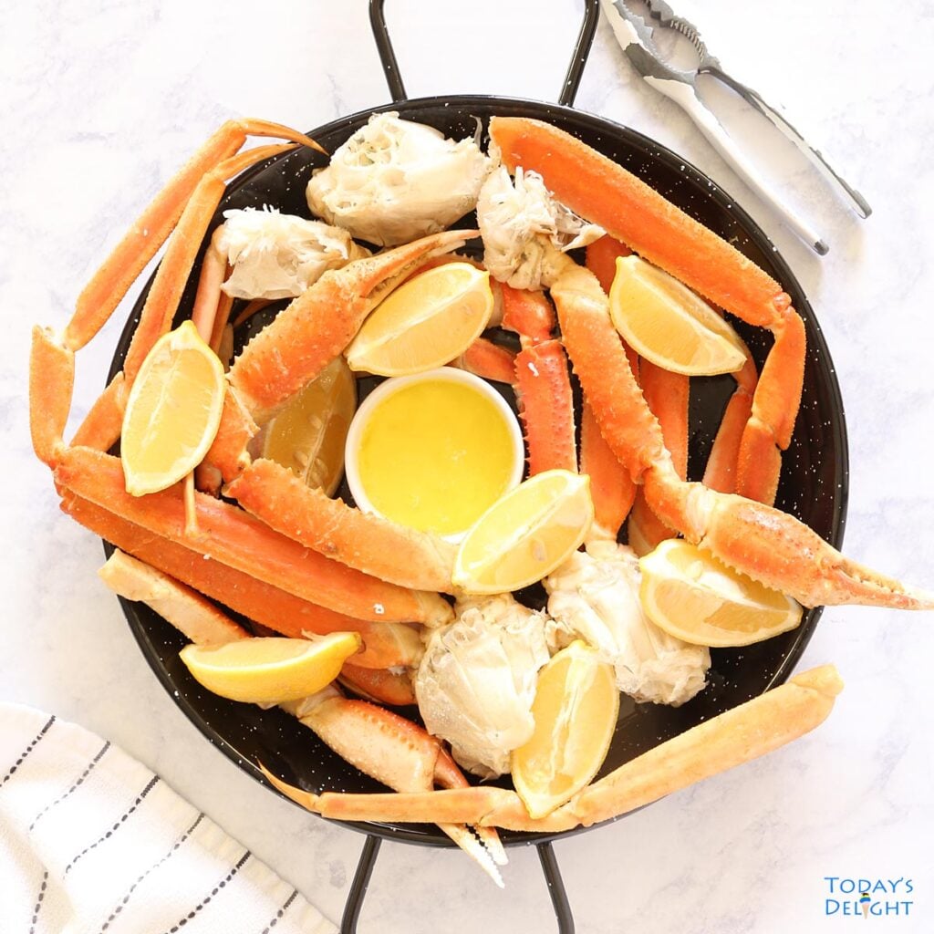 Two pounds of snow crab legs in a platter with melted butter and lemon wedges.