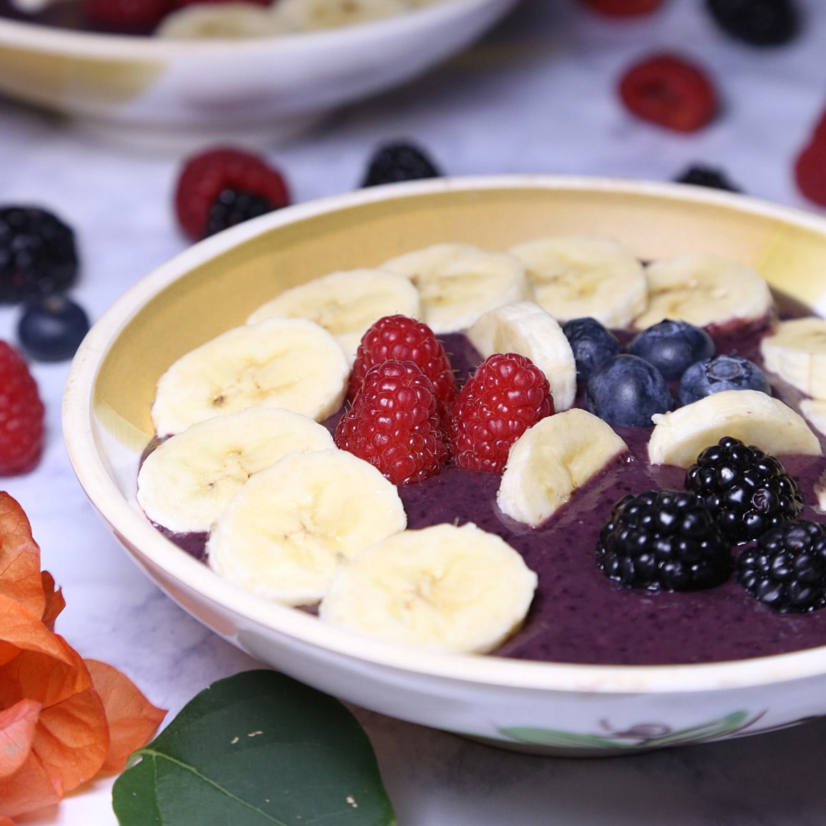 Two acai bowls with pieces of blackberries, blueberries, raspberries and sliced bananas.