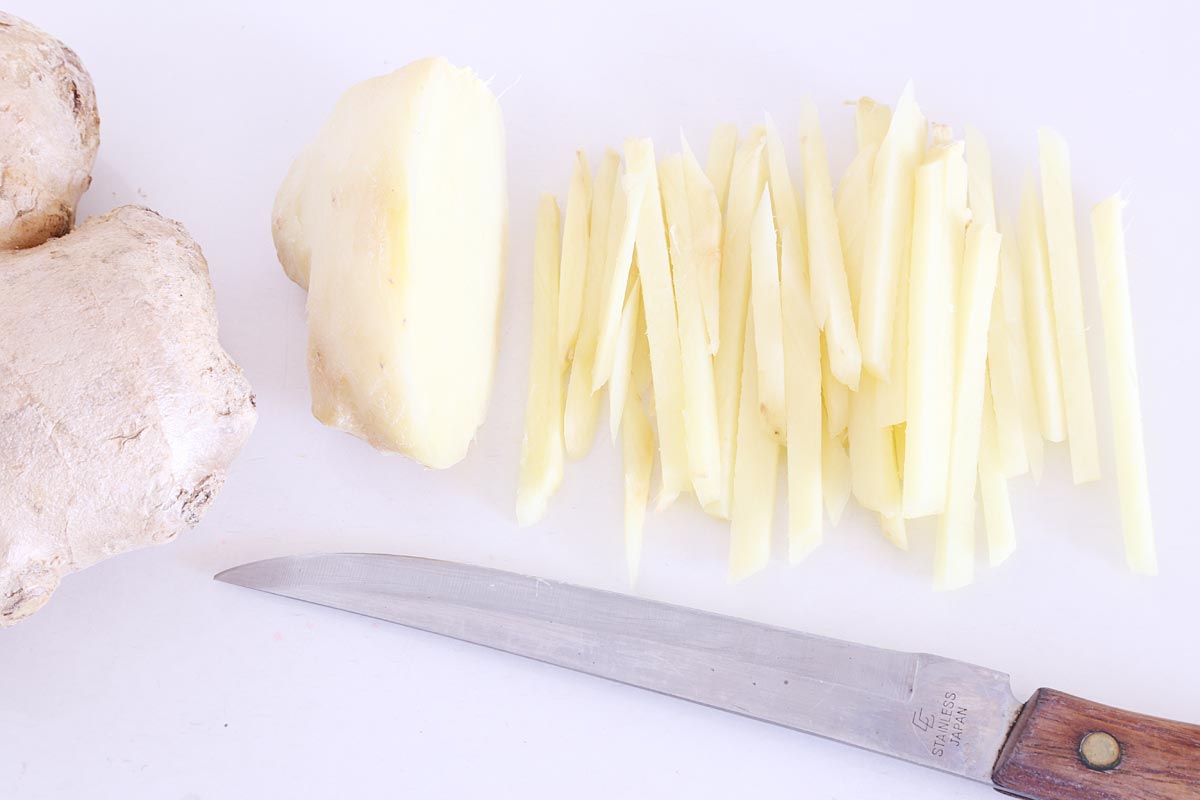 Unpeeled and peeled ginger root sliced with a knife into matchstick-like pieces.