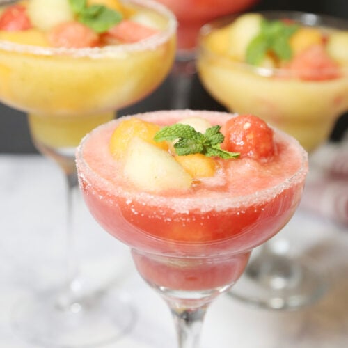 Four melon ball drinks in margarita glasses rimmed with salt. Drinks are made with cantaloupe, honeydew and watermelon garnished with mint leaves.