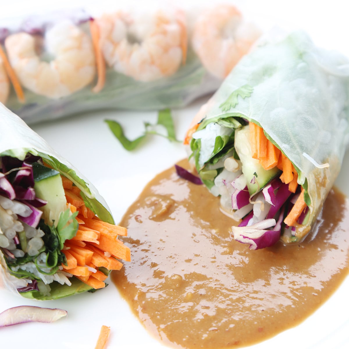 One piece vegetable and shrimp spring roll and another one cut in half laying on peanut sauce on a plate.