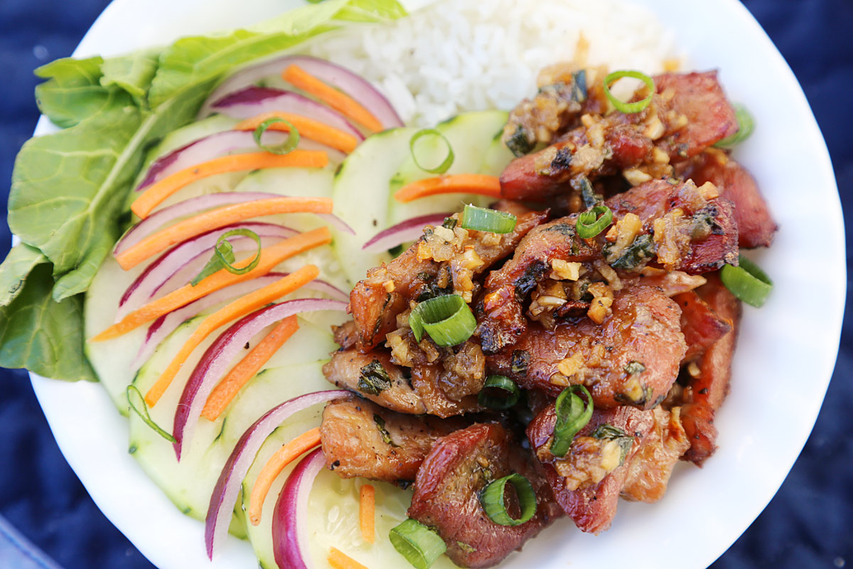 A bowl of Vietnamese grilled pork with rice noodles, thinly sliced carrots and red onions, cucumber, napa leaf, sprinkled with green onions.
