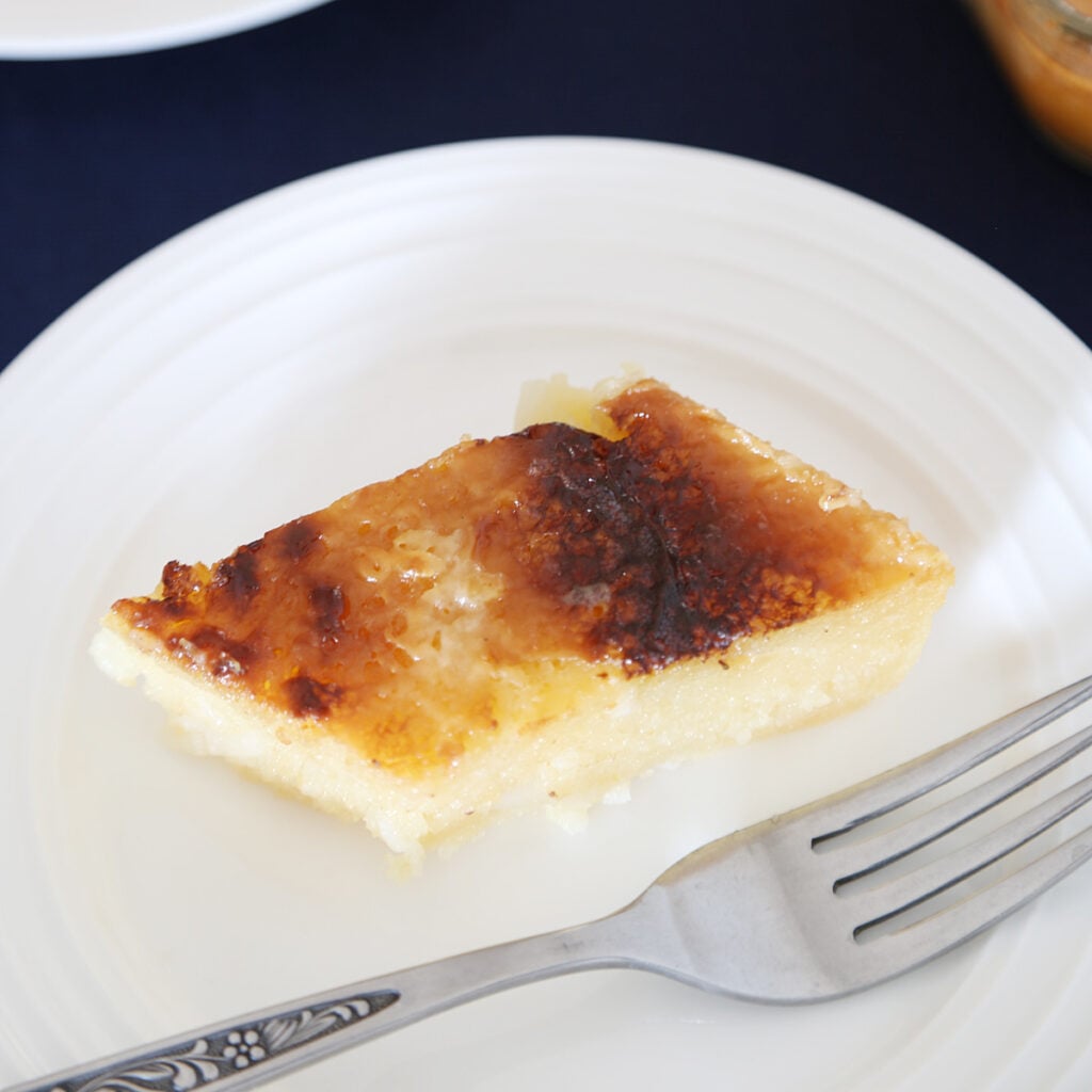 A slice of cassava cake, a Filipino dessert with sweet golden to dark brown topping on a plate with a fork.