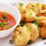 Eight crispy breaded shrimp on a platter with a side of sweet and sour sauce on a small bowl, and both are garnished with green onions.