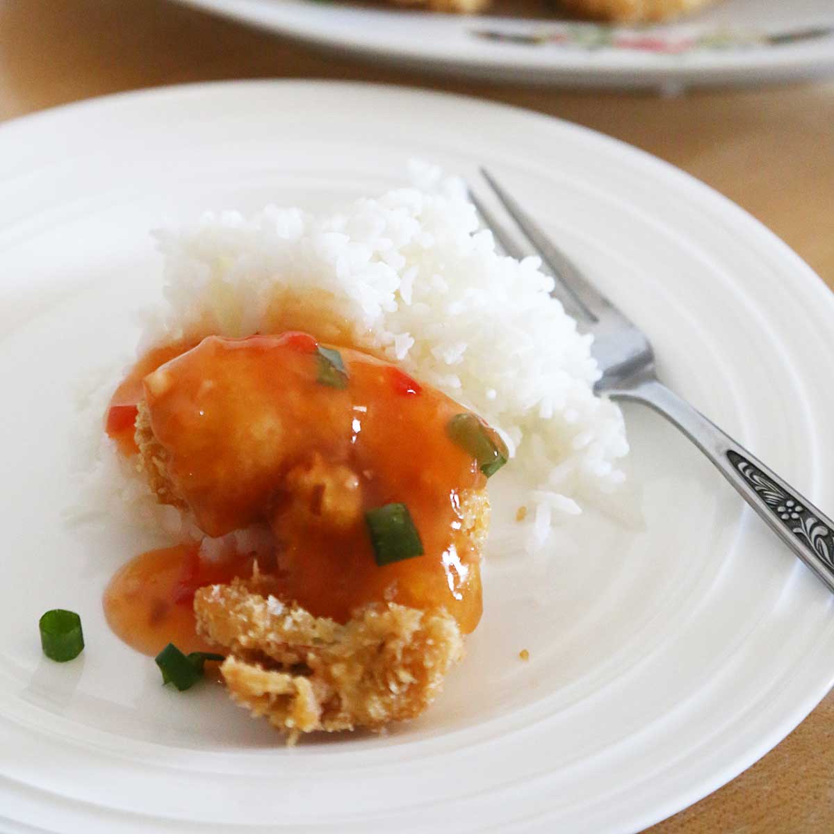 A crispy breaded shrimp garnished with green onion and rice on a plate with a fork.