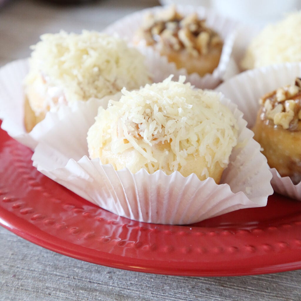 Three ensaymada sweet rolls topped with butter, sugar, and grated cheese and two cinnamon topped with nuts on cupcake liners are on a plate.