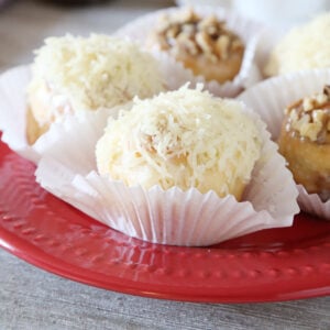 Three ensaymada sweet rolls topped with butter, sugar, and grated cheese and two cinnamon topped with nuts on cupcake liners are on a plate.