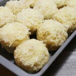 A baking pan of 12 ensaymada, a Filipino brioche bread topped with butter, sugar, and grated cheese.