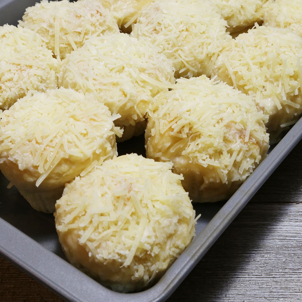 A baking pan of 12 ensaymada, a Filipino brioche bread topped with butter, sugar, and grated cheese.