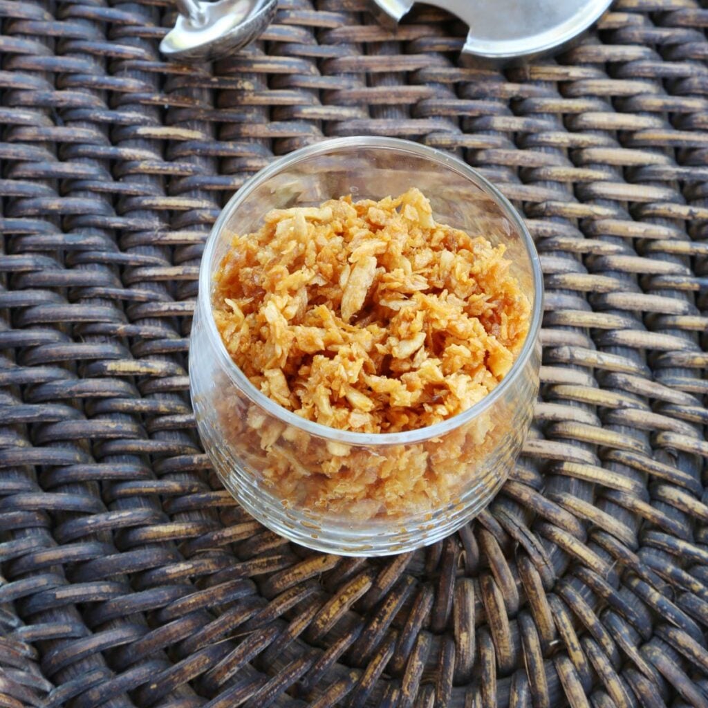 Toasted garlic in a small glass cup with a small spoon and cover on a wooden tray.