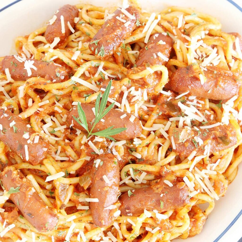 Spaghetti with whole little smokies sausages garnished with grated cheese and chopped parsley on a platter.