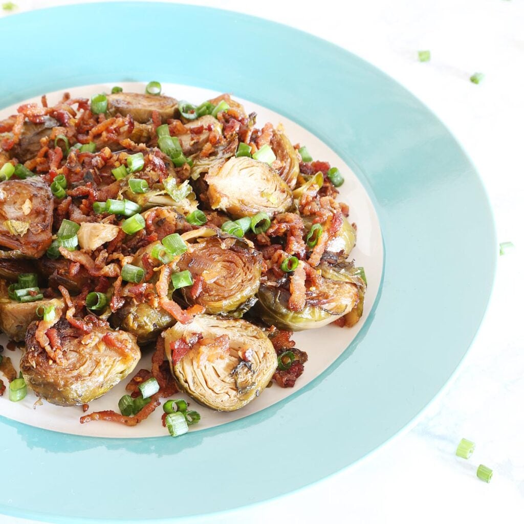 One serving of Brussel sprouts with bacon bits garnished with chopped green onions on a light blue plate.