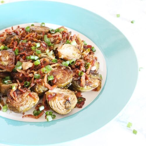 One serving of Brussel sprouts with bacon bits garnished with chopped green onions on a light blue plate.