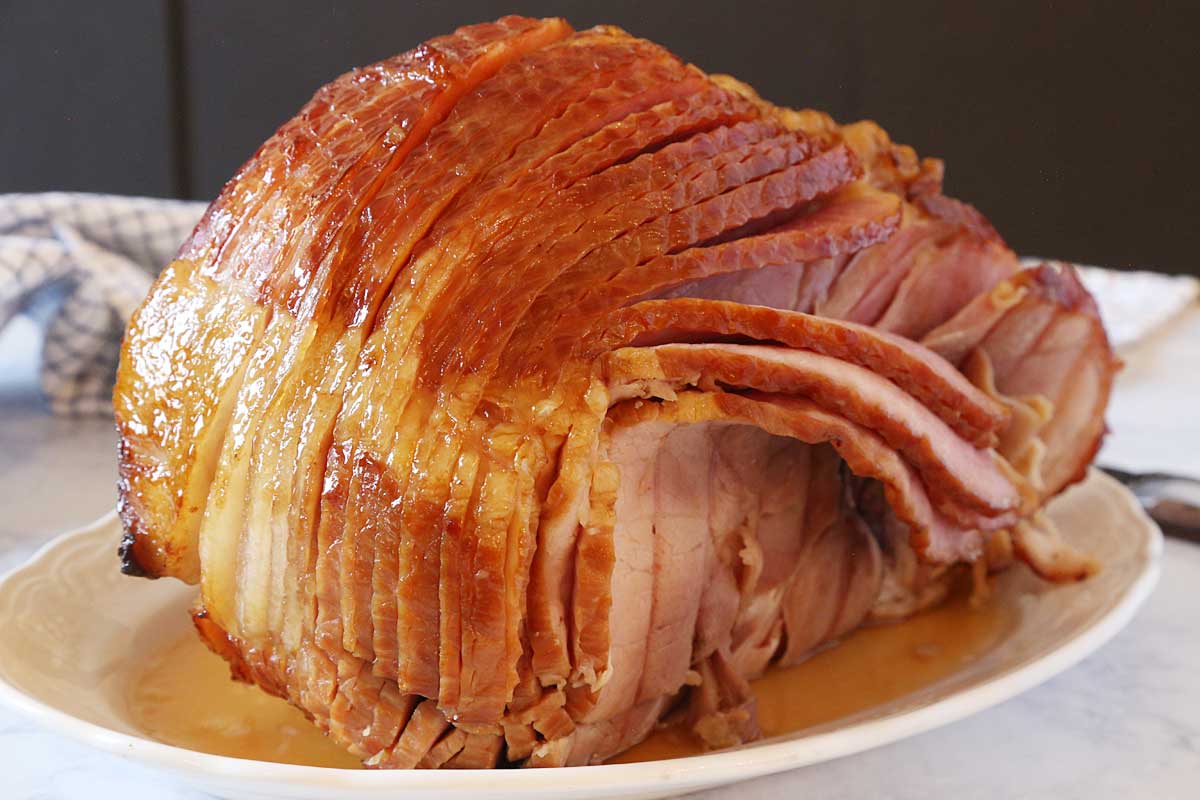 Baked spiral cut ham glazed with honey and spices with syrup on a platter.